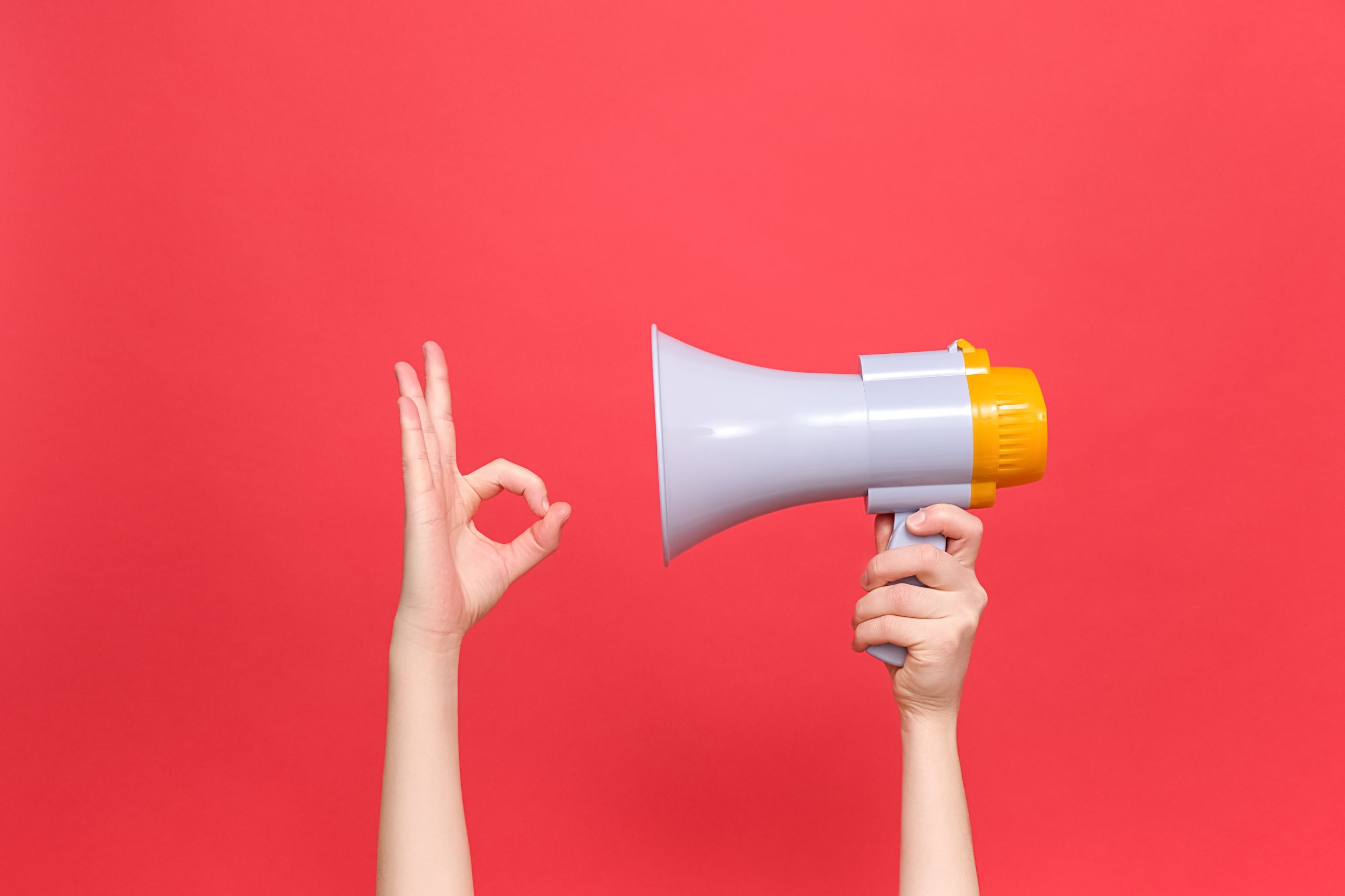Female hands holding megaphone, confident doing ok gesture, gives approval or recommendation, likes idea, isolated over red color background wall with copy space for advertisement. Success concept