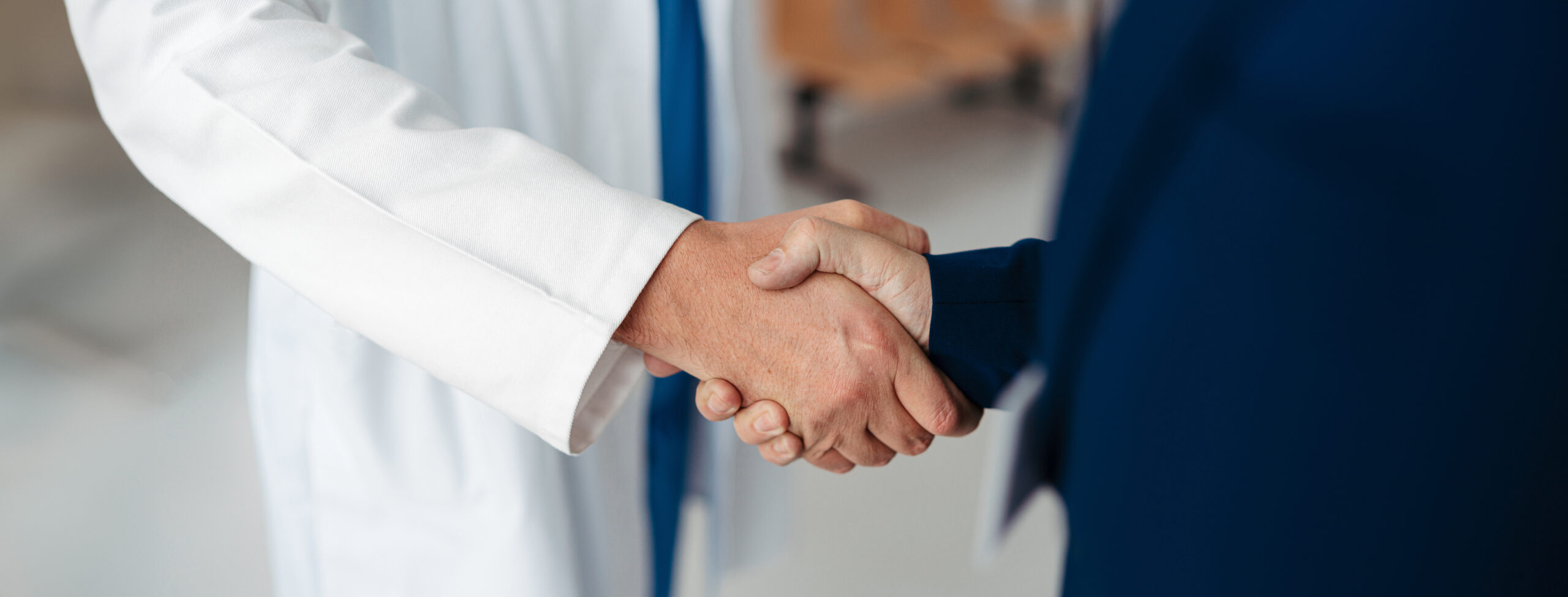 Close up of pharmaceutical sales representative shaking hands with doctor in medical building. Doctor greeting hospital director, manager in private clinic. Banner with copy space.